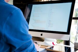 A software developer writing code on a large monitor in a modern office environment
