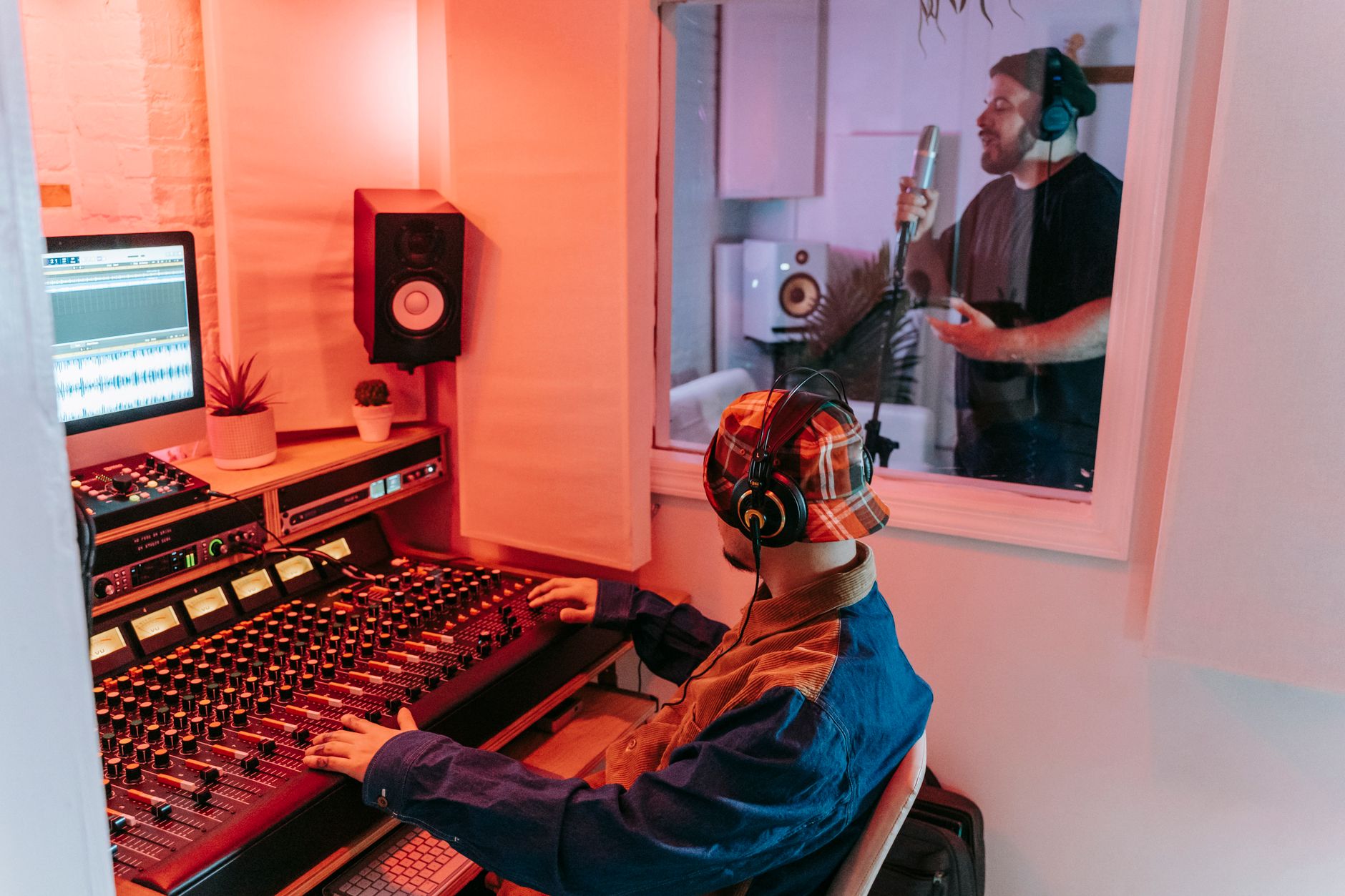 A music producer working at a studio workstation with headphones and software open on screen