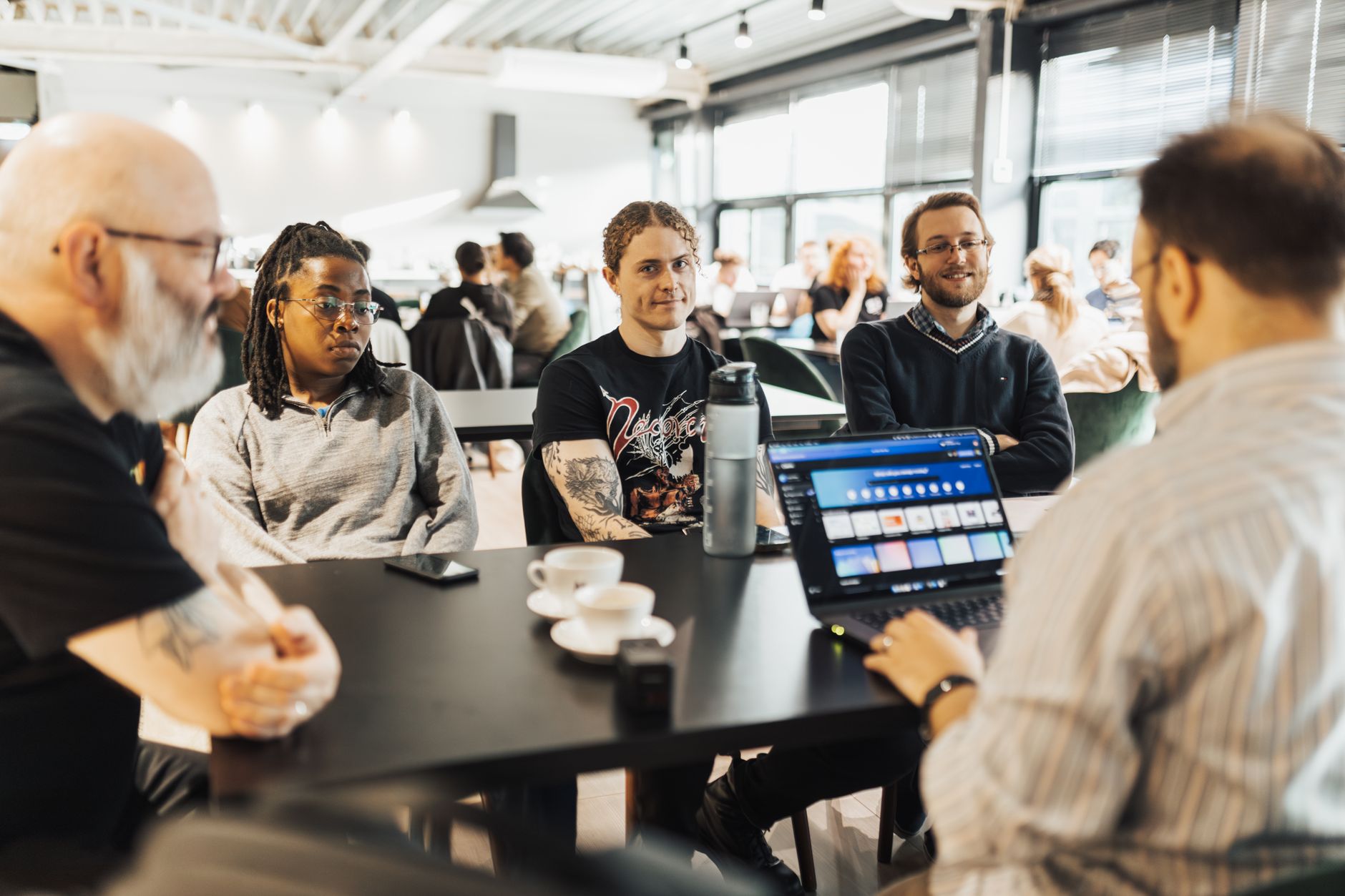 Engineering team gathered around a table reviewing code on a laptop during a standup meeting